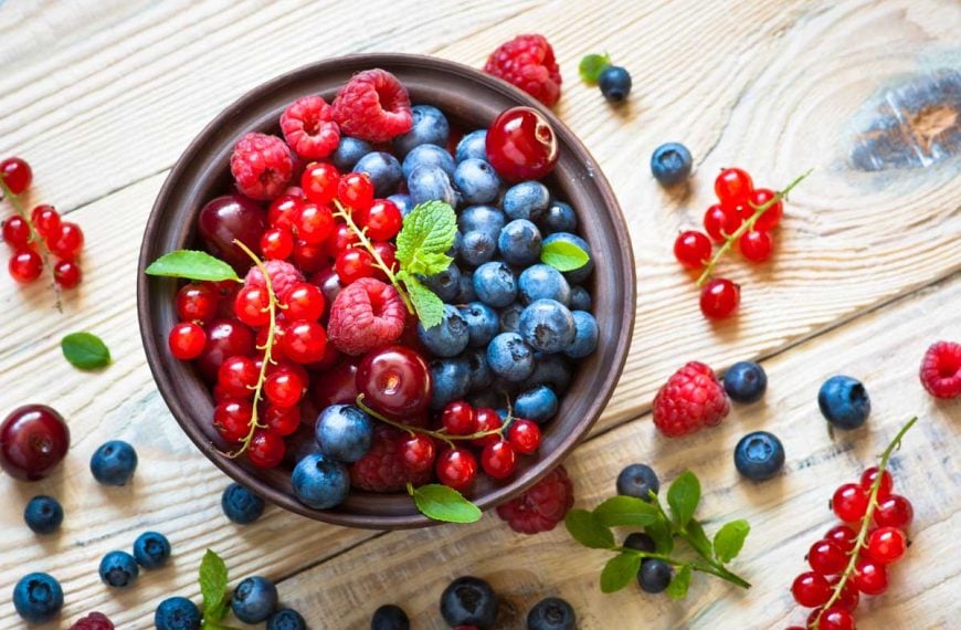 Top-down view of various summer berries in a bowl on a rustic wooden table.