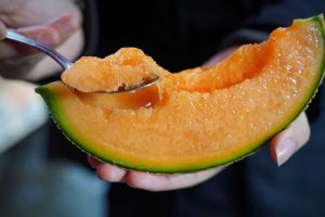 A human hand using a spoon to take a scoop out of a slice of a Yubari king melon.