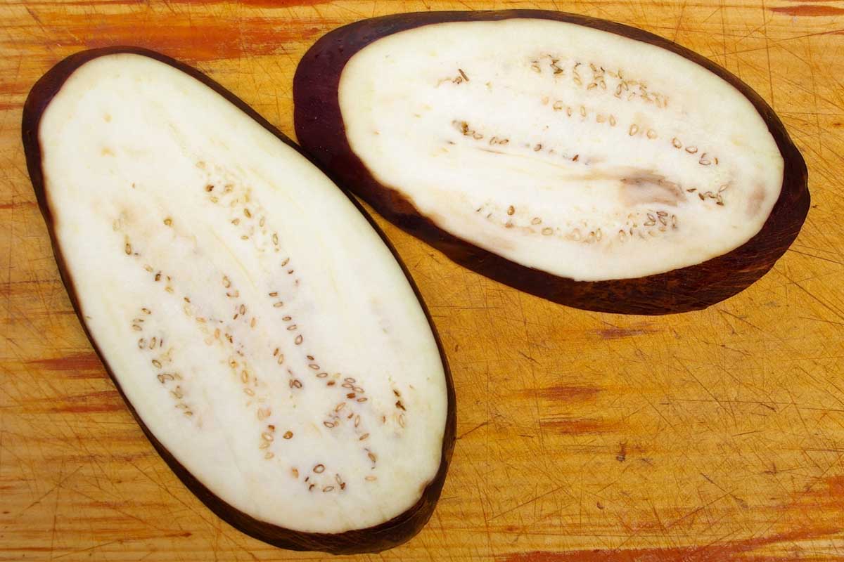 Purple eggplant slices with exposed seeds laid out on a wooden cutting board.