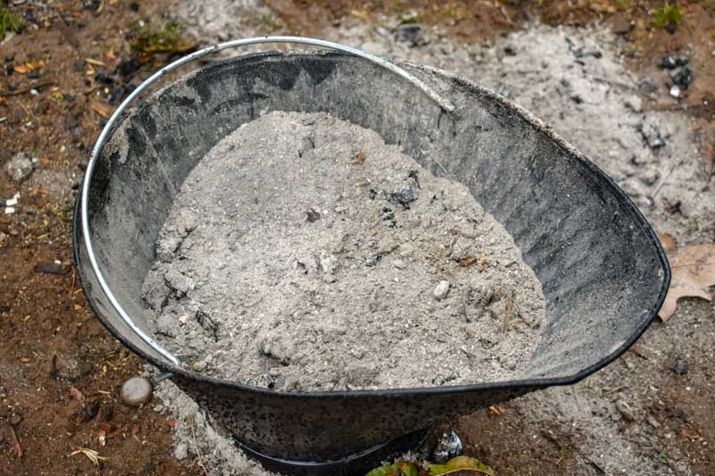 A bucket of wood ashes sitting on bare garden soil.